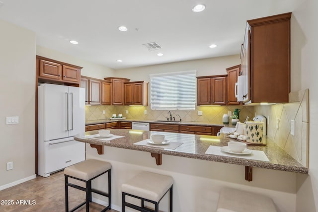 kitchen featuring a kitchen bar, sink, white appliances, and kitchen peninsula