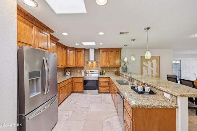 kitchen featuring wall chimney range hood, sink, a breakfast bar area, appliances with stainless steel finishes, and kitchen peninsula