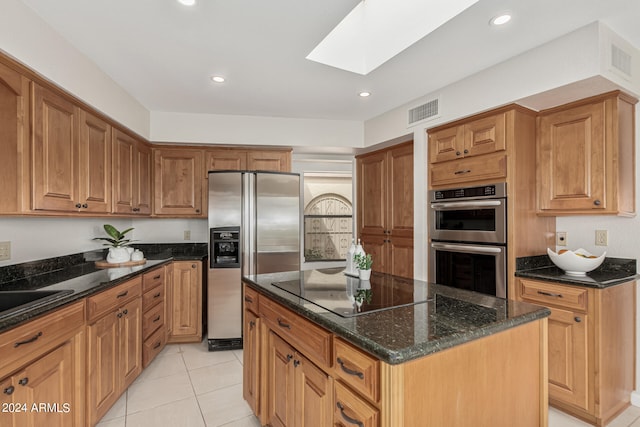 kitchen featuring a skylight, light tile patterned floors, stainless steel appliances, a center island, and dark stone counters