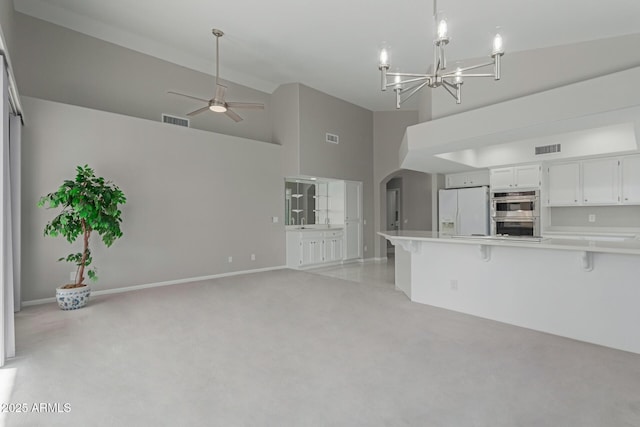 unfurnished living room featuring light carpet, ceiling fan with notable chandelier, and high vaulted ceiling