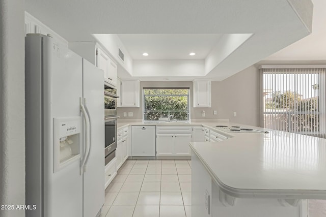 kitchen featuring white appliances, white cabinetry, a raised ceiling, kitchen peninsula, and light tile patterned flooring