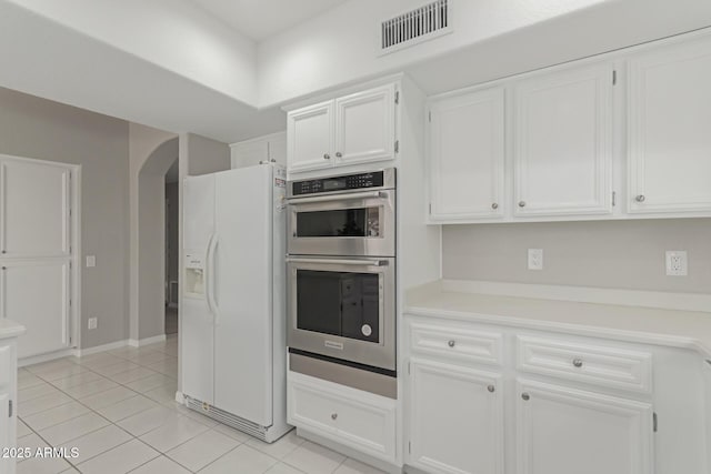 kitchen featuring light tile patterned floors, white fridge with ice dispenser, white cabinets, and double oven