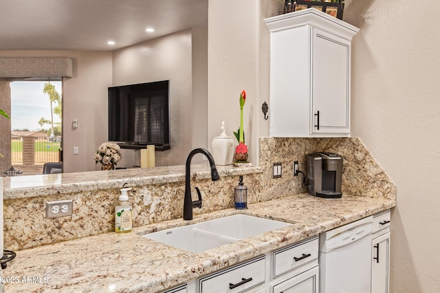 kitchen featuring light stone counters, white cabinets, white dishwasher, and sink