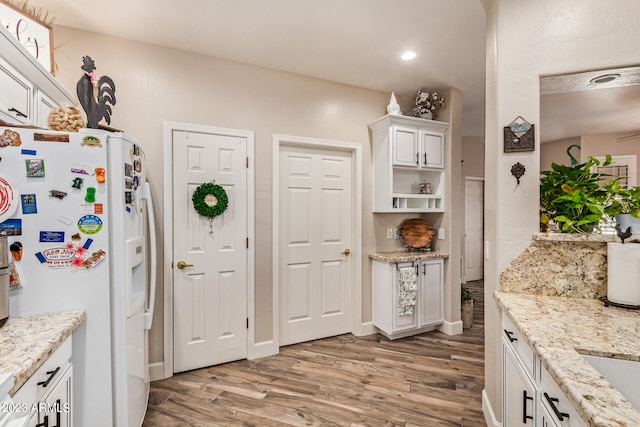 kitchen with light stone countertops, white cabinets, white refrigerator with ice dispenser, and light wood-type flooring