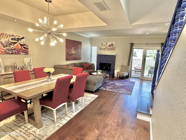 dining area with crown molding, wood-type flooring, visible vents, an inviting chandelier, and a brick fireplace