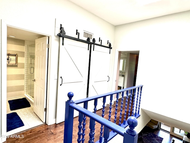 corridor with a barn door, wood finished floors, and an upstairs landing