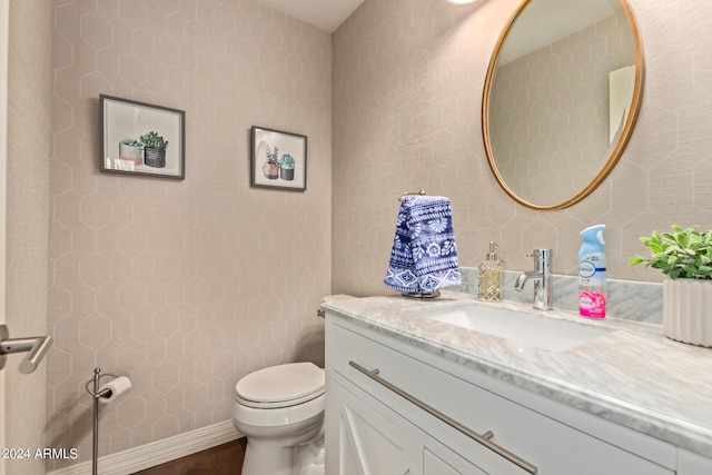 half bathroom with toilet, wallpapered walls, baseboards, and vanity