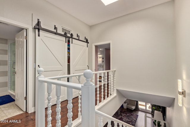 hallway featuring a barn door, wood finished floors, and an upstairs landing