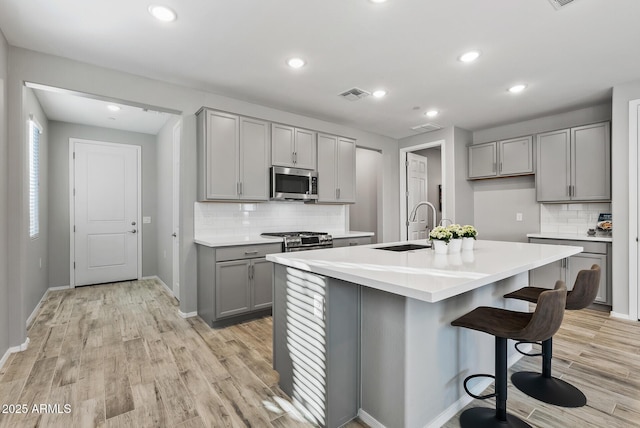 kitchen with appliances with stainless steel finishes, gray cabinetry, light hardwood / wood-style floors, and a center island with sink