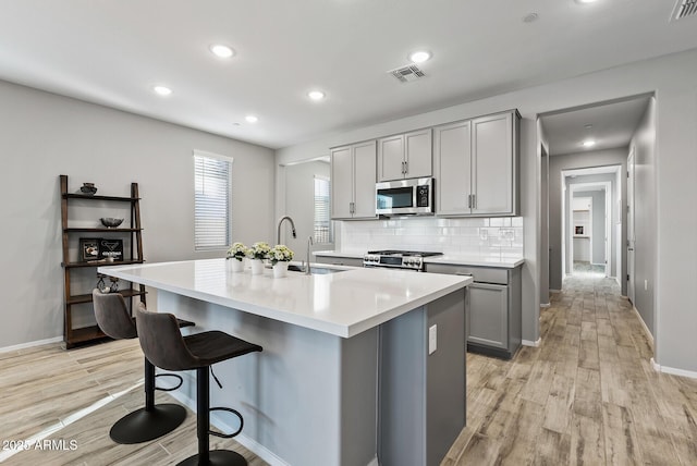 kitchen with an island with sink, light wood-type flooring, gray cabinetry, and stainless steel appliances