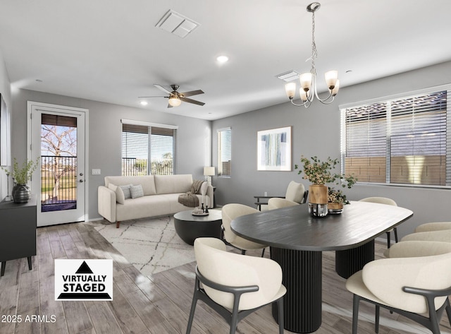 dining space with ceiling fan with notable chandelier and light hardwood / wood-style flooring