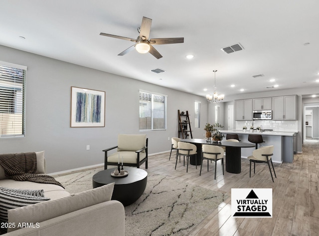 living room with ceiling fan with notable chandelier and light hardwood / wood-style flooring