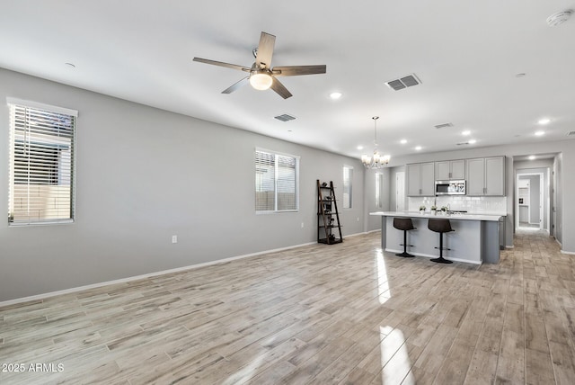 kitchen featuring a kitchen island with sink, gray cabinetry, hanging light fixtures, a breakfast bar, and tasteful backsplash