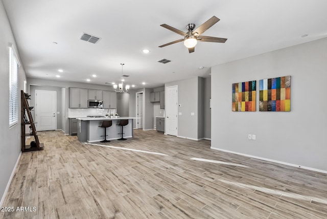 kitchen featuring a kitchen island with sink, gray cabinets, a breakfast bar area, pendant lighting, and decorative backsplash