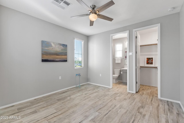 unfurnished bedroom featuring a closet, ensuite bath, ceiling fan, a walk in closet, and light hardwood / wood-style flooring