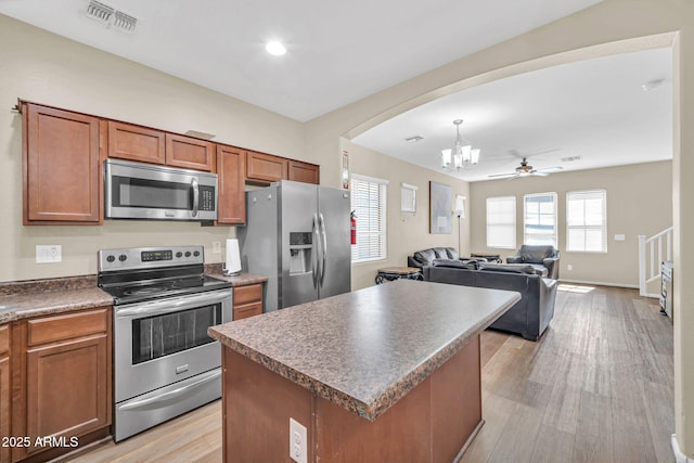 2118 N 77th Ln, Phoenix, AZ 85035 - kitchen featuring stainless steel appliances, brown cabinets, a chandelier, arched walkways, and light wood-style flooring