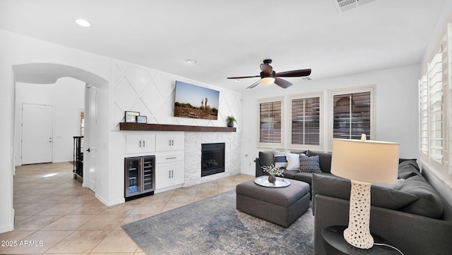 living area featuring arched walkways, a fireplace, light tile patterned floors, a ceiling fan, and beverage cooler