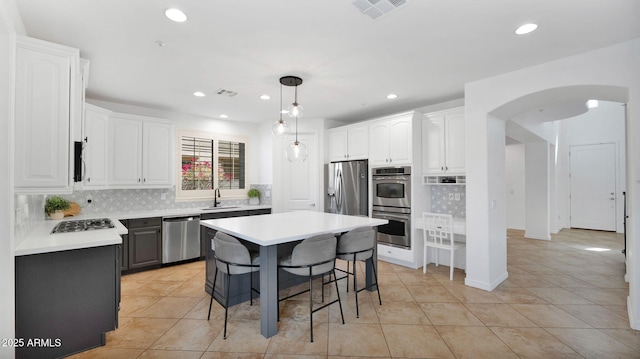 kitchen featuring visible vents, white cabinets, arched walkways, a breakfast bar area, and stainless steel appliances