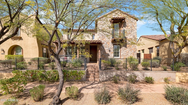 mediterranean / spanish-style home featuring stone siding, a fenced front yard, a tiled roof, and stucco siding