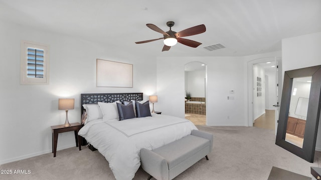 bedroom with baseboards, visible vents, arched walkways, connected bathroom, and light colored carpet