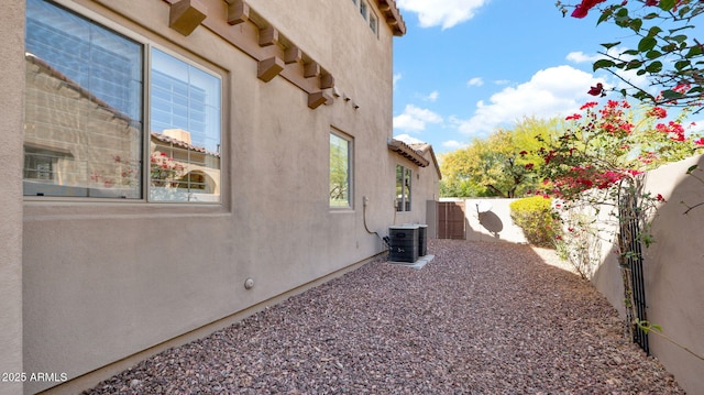 view of side of home with cooling unit, a fenced backyard, and stucco siding