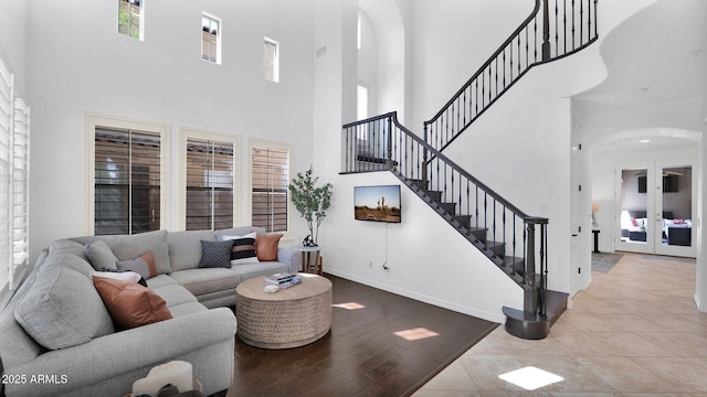 living area featuring baseboards, arched walkways, wood finished floors, a high ceiling, and stairs