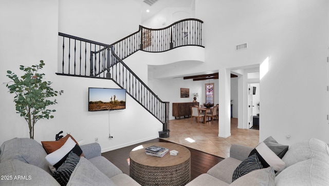 living area with wood finished floors, a towering ceiling, visible vents, stairs, and baseboards