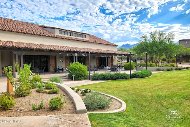 rear view of house with a lawn, a patio area, a tile roof, and stucco siding