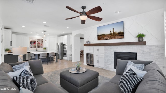 living area featuring arched walkways, light tile patterned floors, a stone fireplace, wine cooler, and visible vents