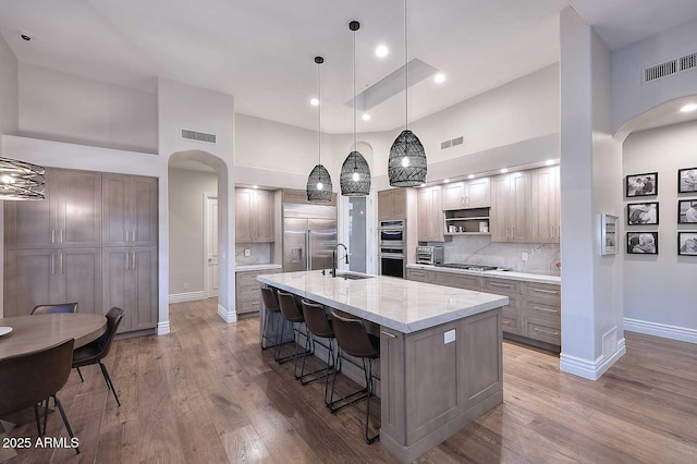 kitchen with light stone countertops, pendant lighting, appliances with stainless steel finishes, decorative backsplash, and a center island with sink