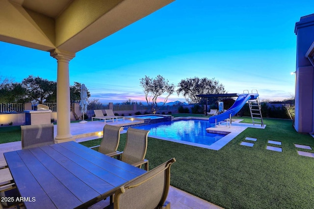 pool at dusk with an in ground hot tub, a patio area, a water slide, and a yard