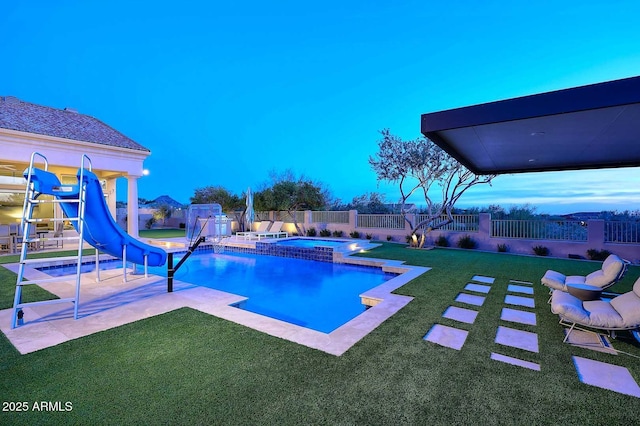 pool at dusk featuring an in ground hot tub, a patio, a lawn, and a water slide