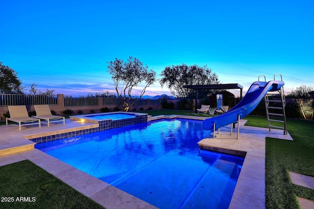 pool at dusk featuring an in ground hot tub, a yard, a water slide, and a patio