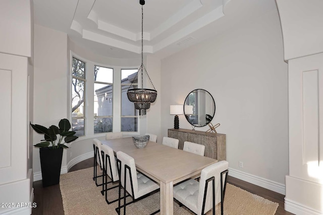 dining space featuring dark wood-type flooring, an inviting chandelier, and a raised ceiling