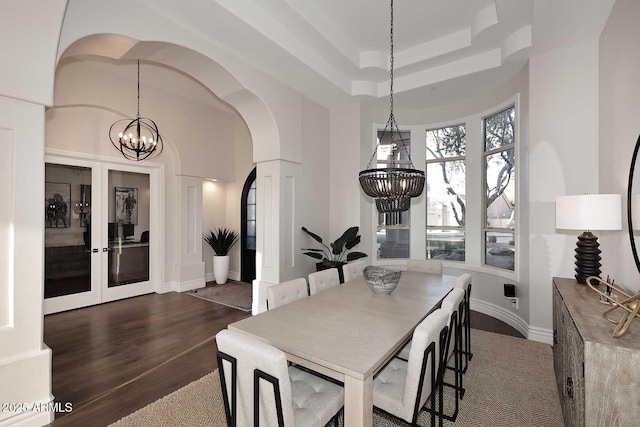 dining space featuring dark hardwood / wood-style floors, a raised ceiling, french doors, and an inviting chandelier