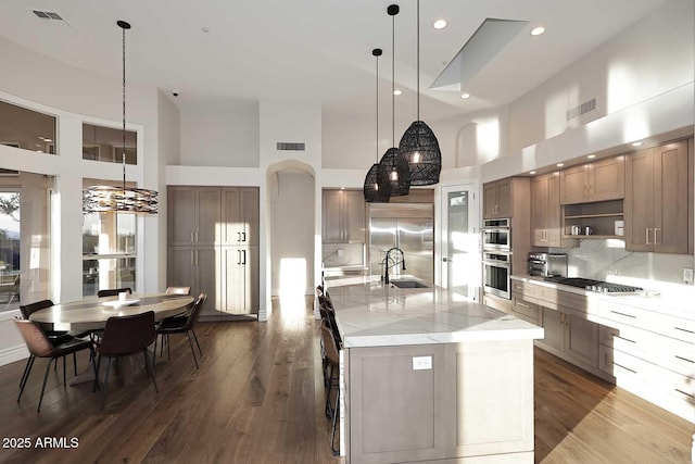 kitchen with decorative light fixtures, a high ceiling, appliances with stainless steel finishes, and a spacious island