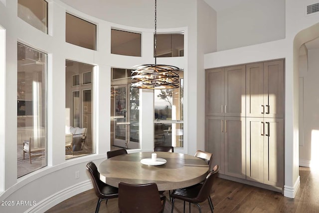 dining room with a towering ceiling, a notable chandelier, and dark hardwood / wood-style flooring