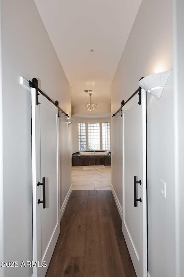 corridor featuring dark hardwood / wood-style flooring, a barn door, and vaulted ceiling