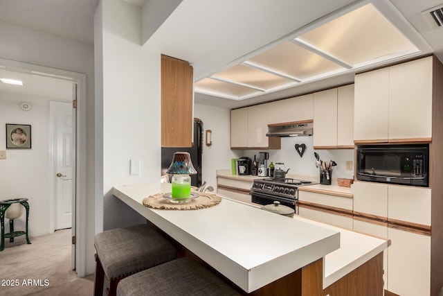 10410 N Cave Creek Rd Unit 2030, Phoenix, AZ 85020 - kitchen featuring black appliances, under cabinet range hood, a peninsula, light colored carpet, and a breakfast bar