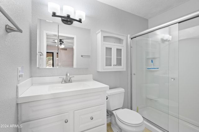 bathroom featuring a shower with door, toilet, vanity, ceiling fan, and a textured ceiling