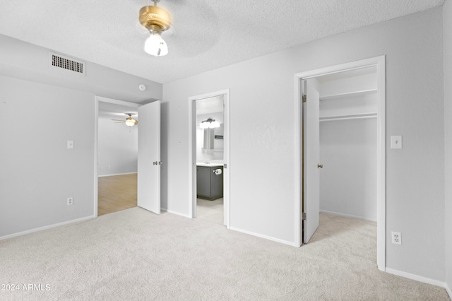 unfurnished bedroom featuring ceiling fan, a walk in closet, light carpet, and ensuite bath