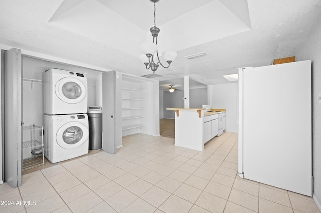 clothes washing area with ceiling fan with notable chandelier, light tile patterned floors, a textured ceiling, and stacked washer / drying machine