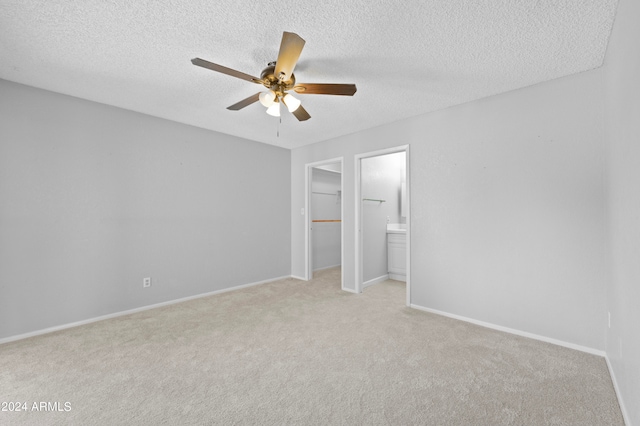 unfurnished bedroom with light carpet, a textured ceiling, ceiling fan, a closet, and ensuite bathroom