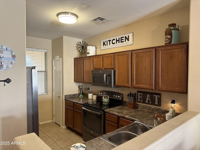 kitchen featuring light tile patterned flooring, a sink, appliances with stainless steel finishes, brown cabinetry, and visible vents