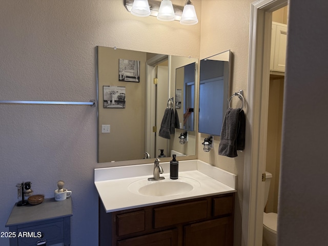 bathroom featuring a textured wall, toilet, and vanity