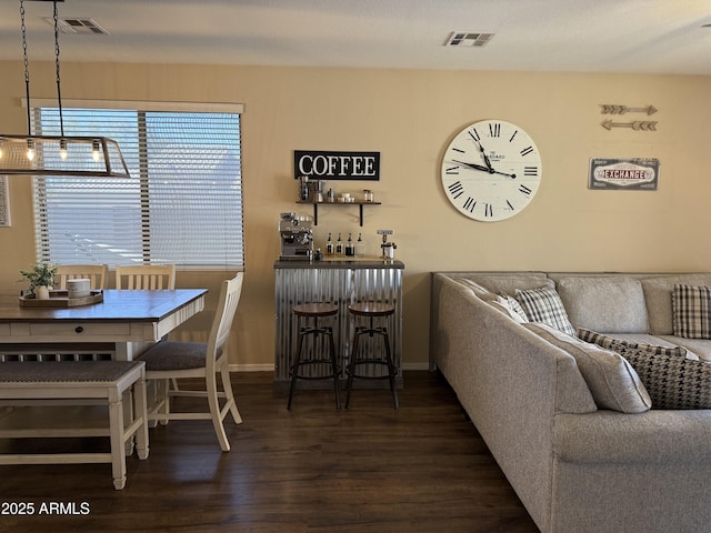 living room featuring wood finished floors, bar area, baseboards, and visible vents