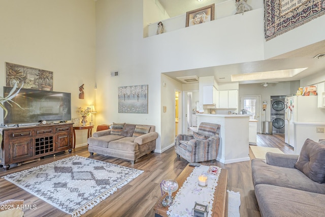 living room with hardwood / wood-style floors, a towering ceiling, and stacked washer and clothes dryer