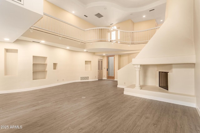 unfurnished living room with a large fireplace, a towering ceiling, built in shelves, and hardwood / wood-style flooring