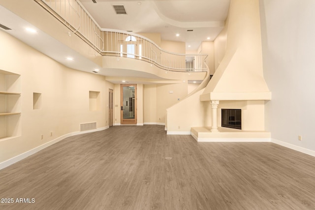 unfurnished living room with hardwood / wood-style floors, a towering ceiling, and a fireplace