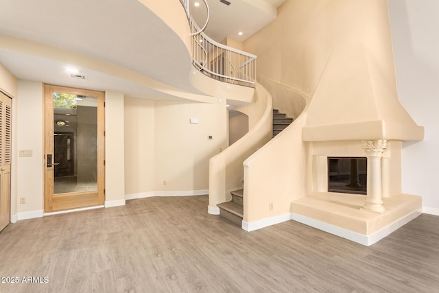 stairs with a high ceiling, wood-type flooring, and a large fireplace